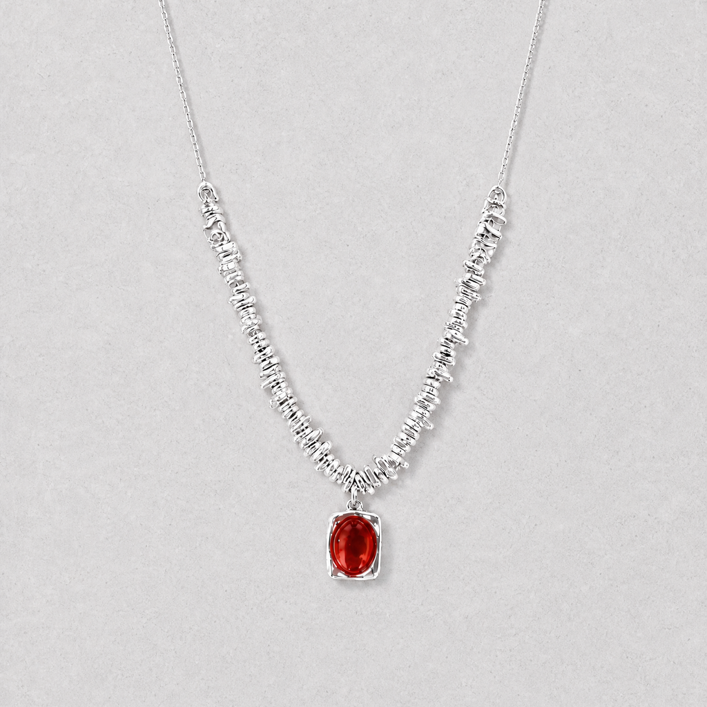A delicate silver necklace featuring a textured, beaded chain and a central oval red agate pendant, displayed against a neutral light gray background.