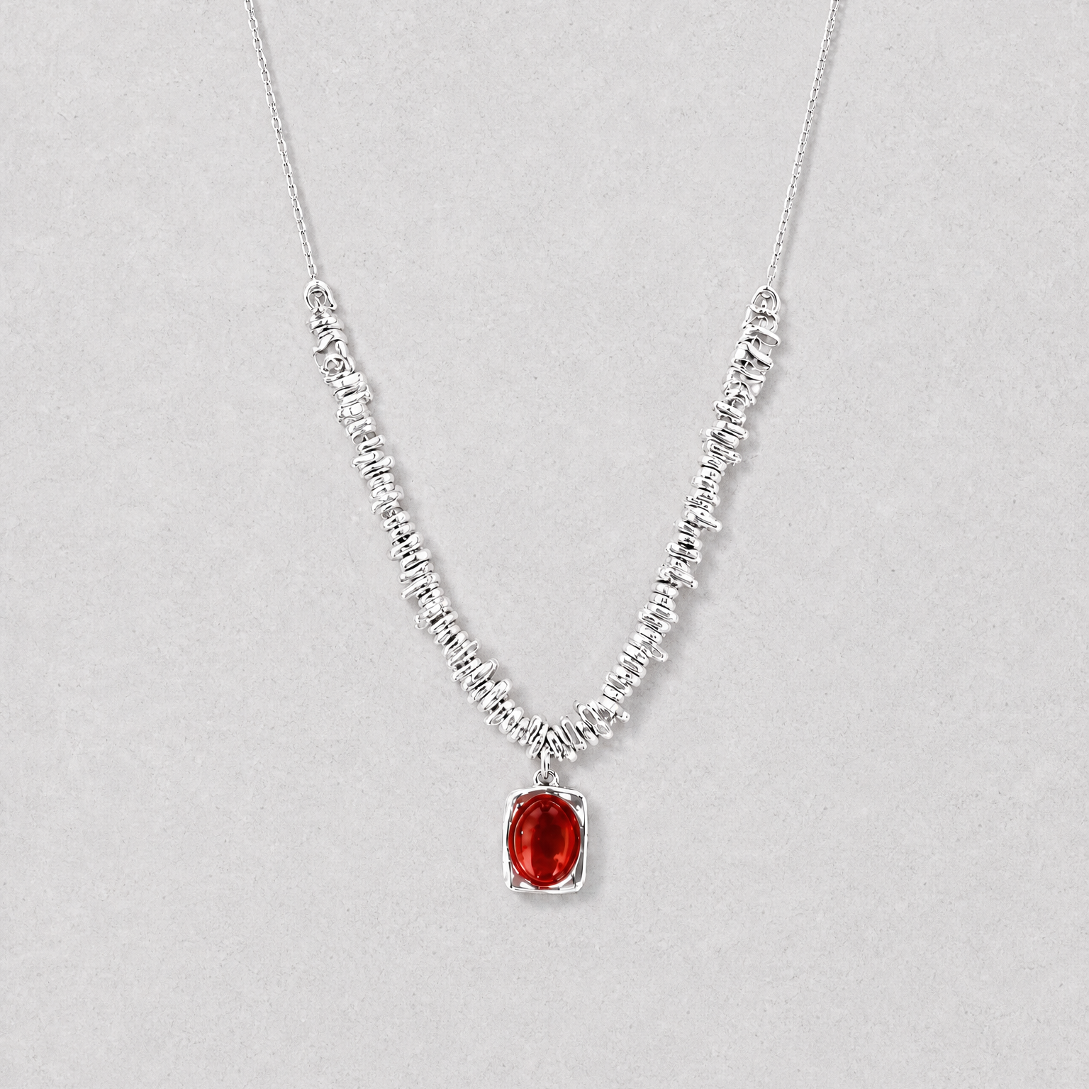 A delicate silver necklace featuring a textured, beaded chain and a central oval red agate pendant, displayed against a neutral light gray background.