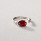 A silver open-band ring featuring a prominent oval cabochon red agate gemstone, photographed on a neutral light gray textured background.