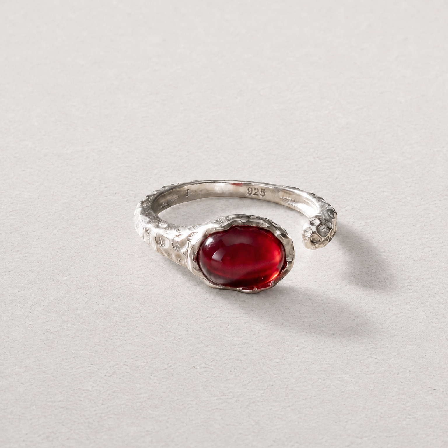 A silver open-band ring featuring a prominent oval cabochon red agate gemstone, photographed on a neutral light gray textured background.