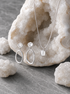 Silver jewelry set with earrings and a necklace on a stone surface