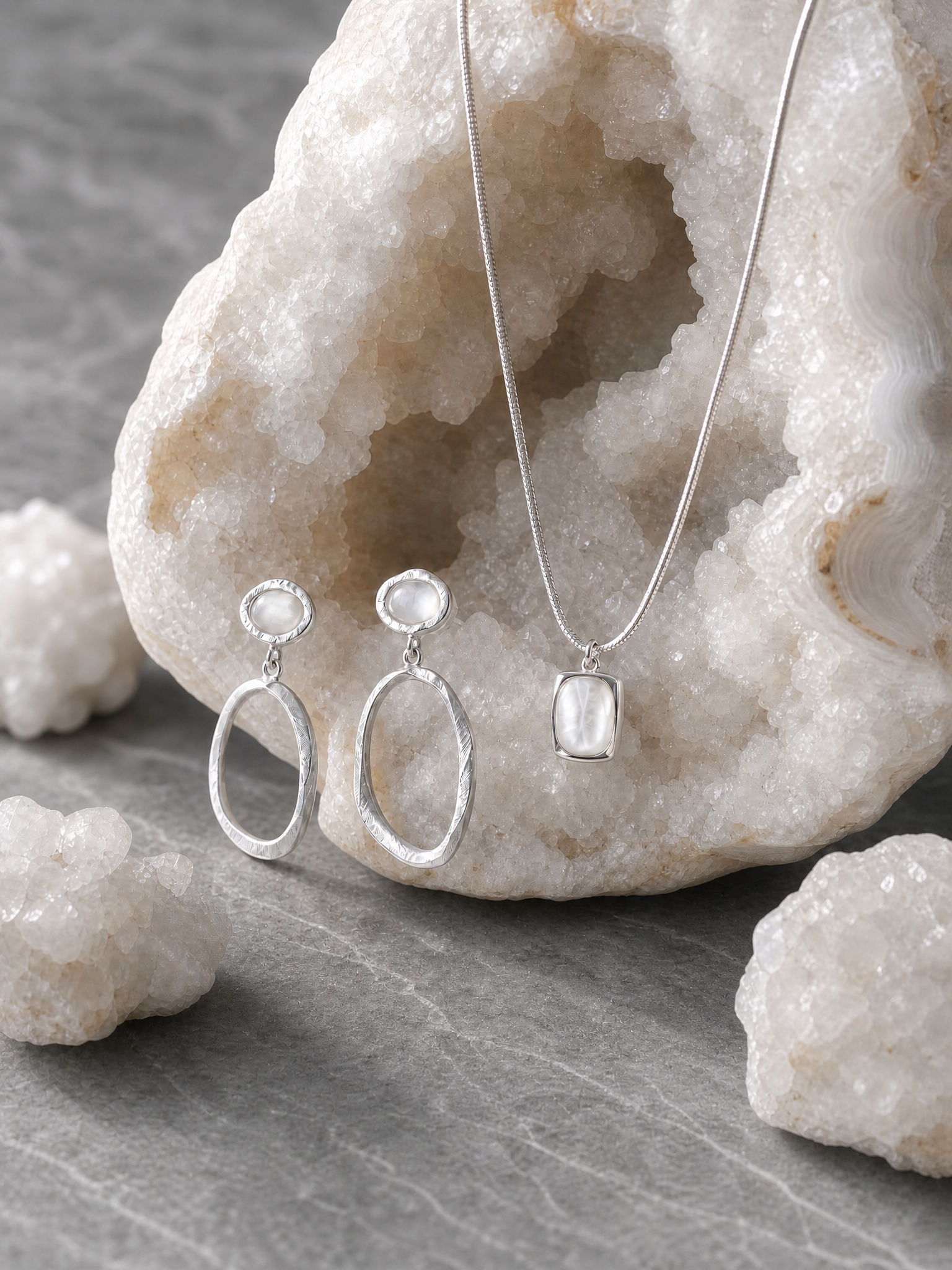 Silver jewelry set with earrings and a necklace on a stone surface