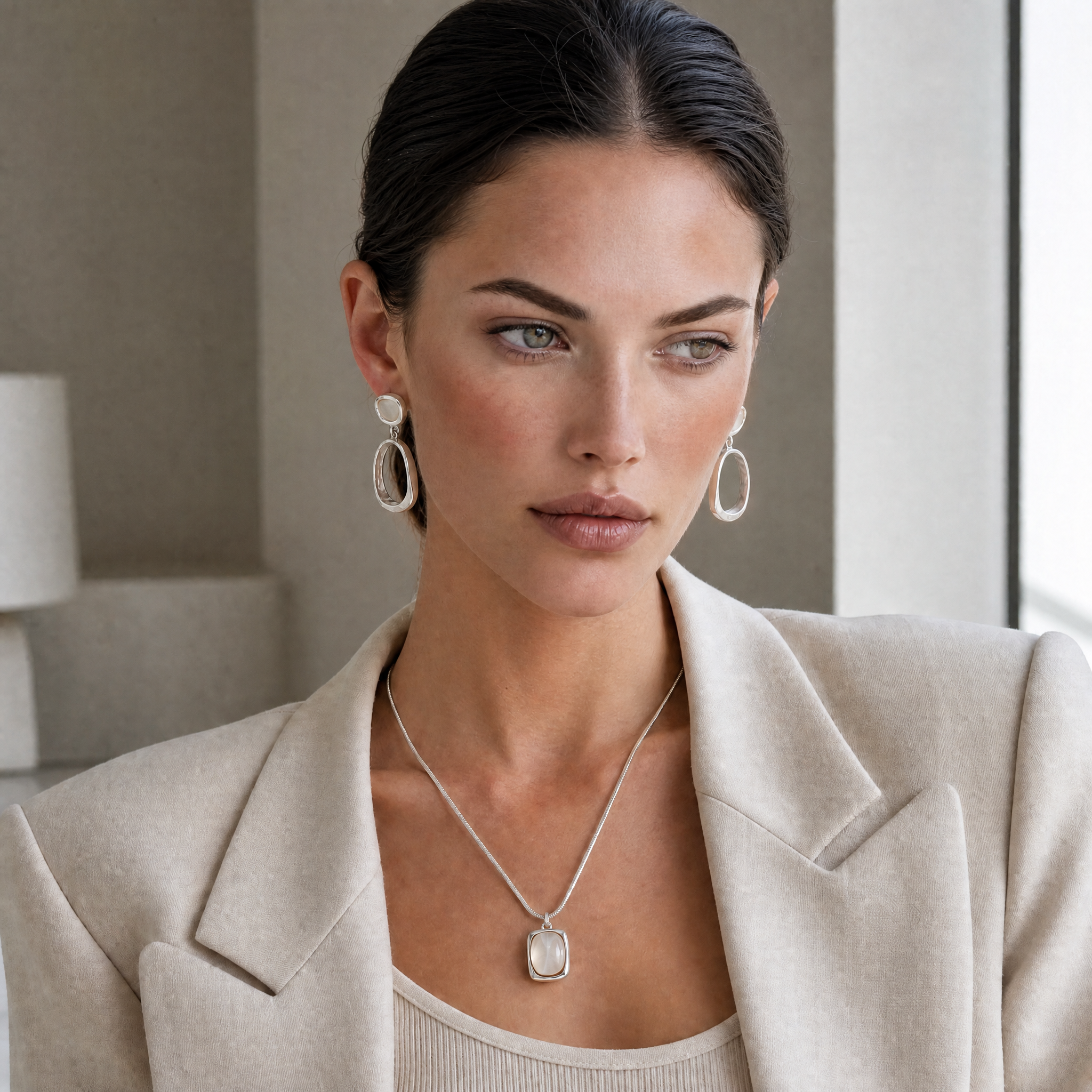 Woman wearing a beige blazer and clarity jewelry set of white agate drop earrings and necklace indoors