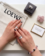 Hands wearing textured silver band rings with a LOEWE pouch and jewelry box in the background, minimalist aesthetic