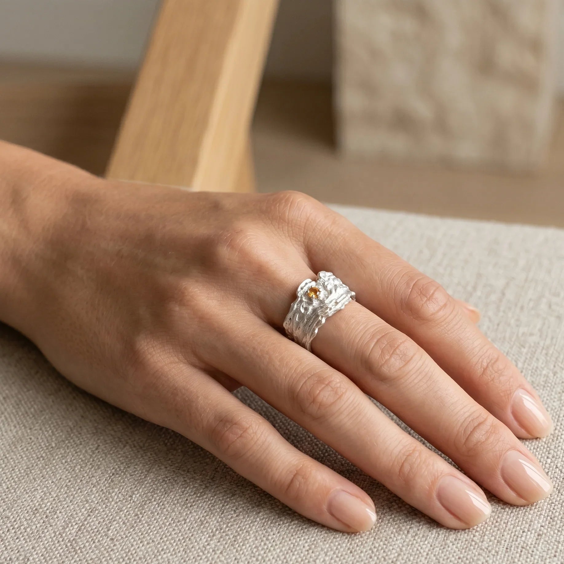 Hand wearing a textured sterling silver crystal ring with minimalist design on neutral fabric
