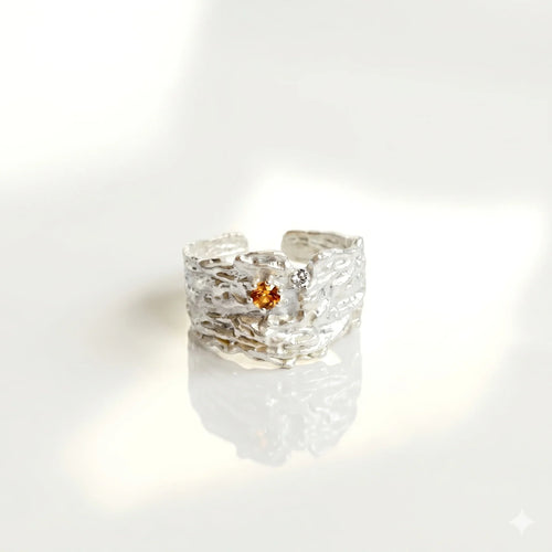 Sterling silver textured ring with orange gemstone on reflective white background