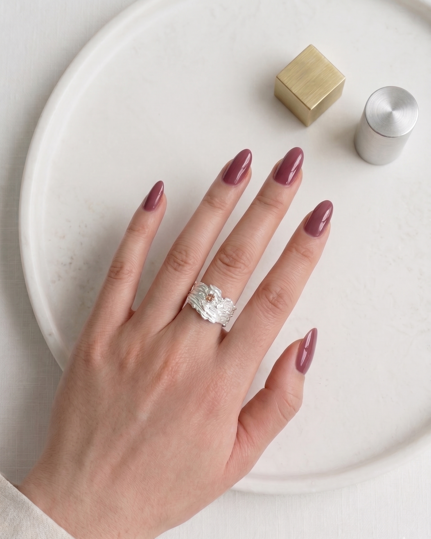 Hand wearing a textured sterling silver crystal ring with minimalist design on white plate