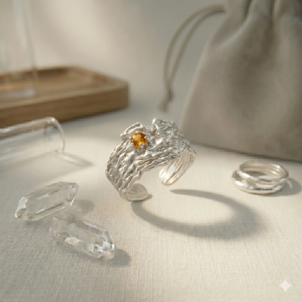 Sterling silver textured ring with yellow gemstone and clear crystals on neutral background.