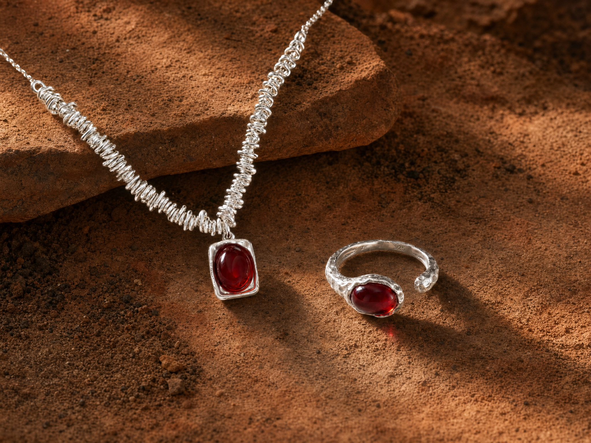 Silver necklace and ring with red gemstones on a textured brown surface