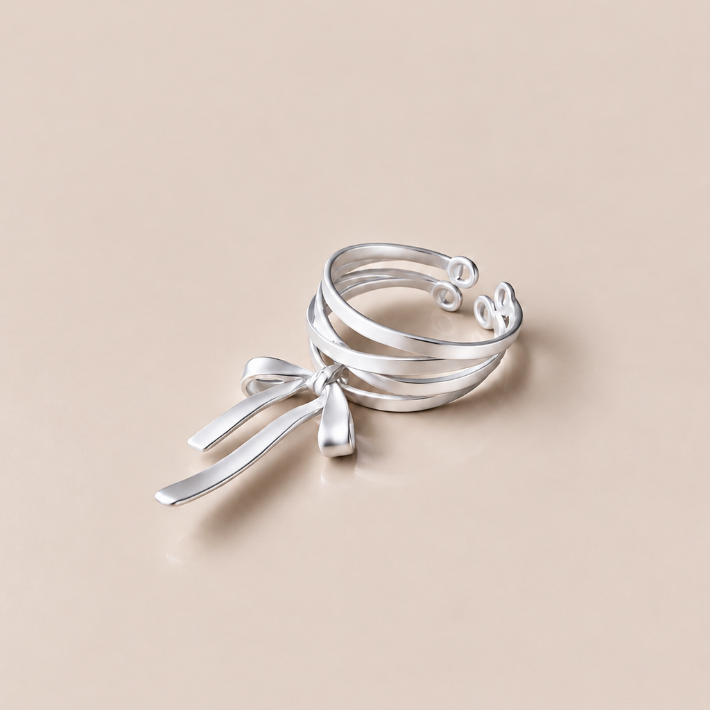 KNOTTED SIGNAL layered sterling silver bow ring on a warm neutral background