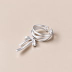 KNOTTED SIGNAL layered sterling silver bow ring on a warm neutral background