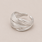 A silver-toned multi-strand twisted ring with an open cuff design, photographed on a solid beige background.