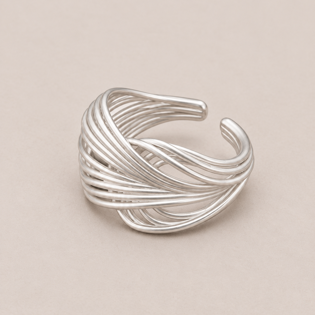 A silver-toned multi-strand twisted ring with an open cuff design, photographed on a solid beige background.