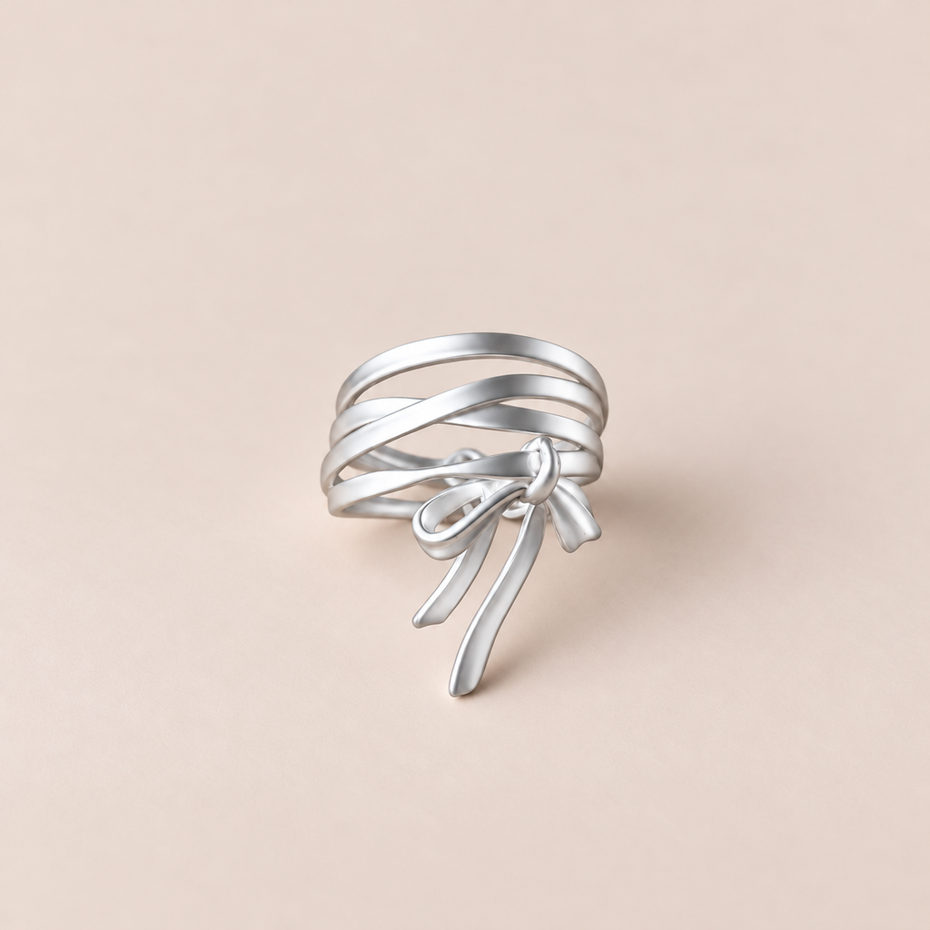 A silver multi-band ring with a delicate bow detail at the center, displayed on a soft beige background.