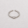 A minimalist silver ring with a small heart charm in the center, displayed on a textured off-white surface.