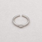 A minimalist silver ring with a small heart charm in the center, displayed on a textured off-white surface.