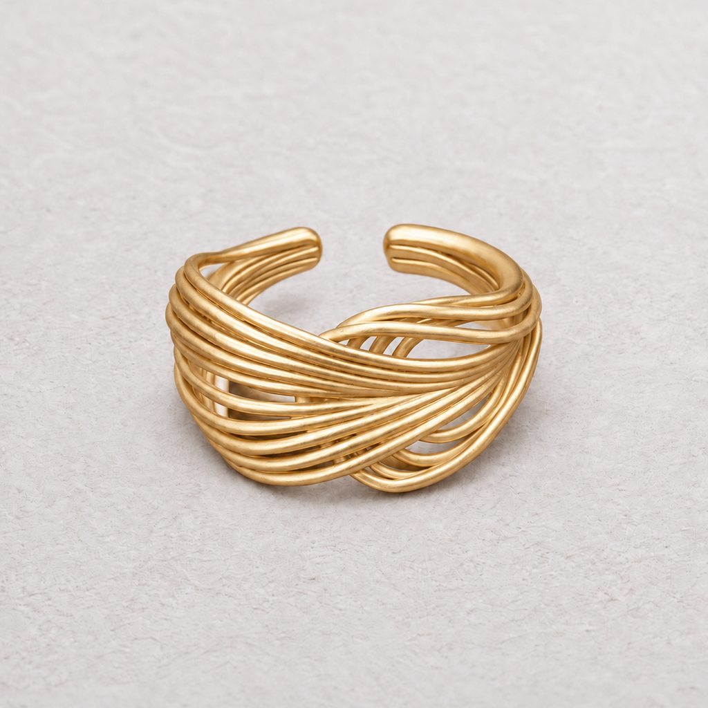 A gold-toned wrap ring with multiple twisted bands, photographed on a light textured neutral background.