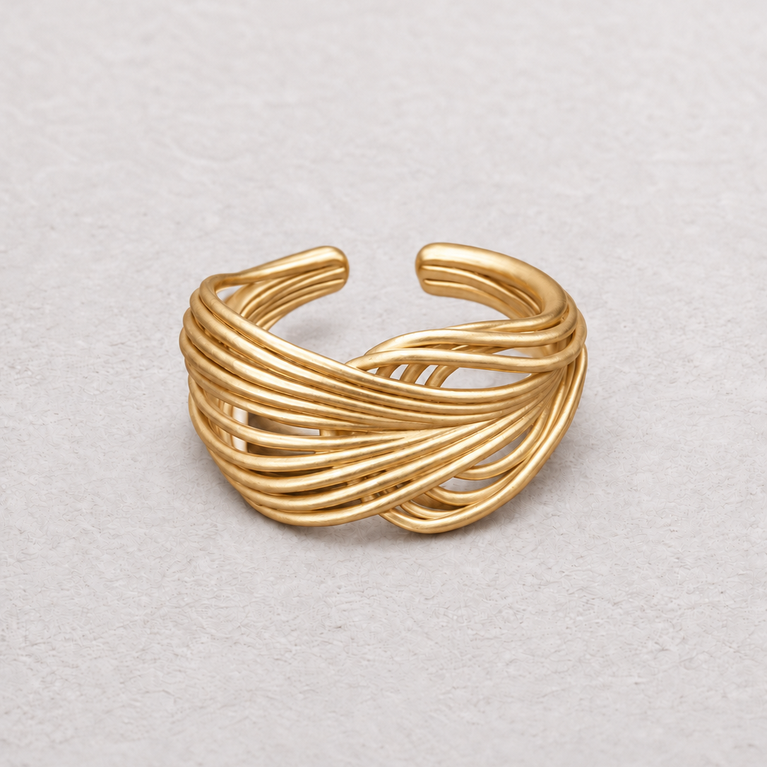 A gold-toned wrap ring with multiple twisted bands, photographed on a light textured neutral background.