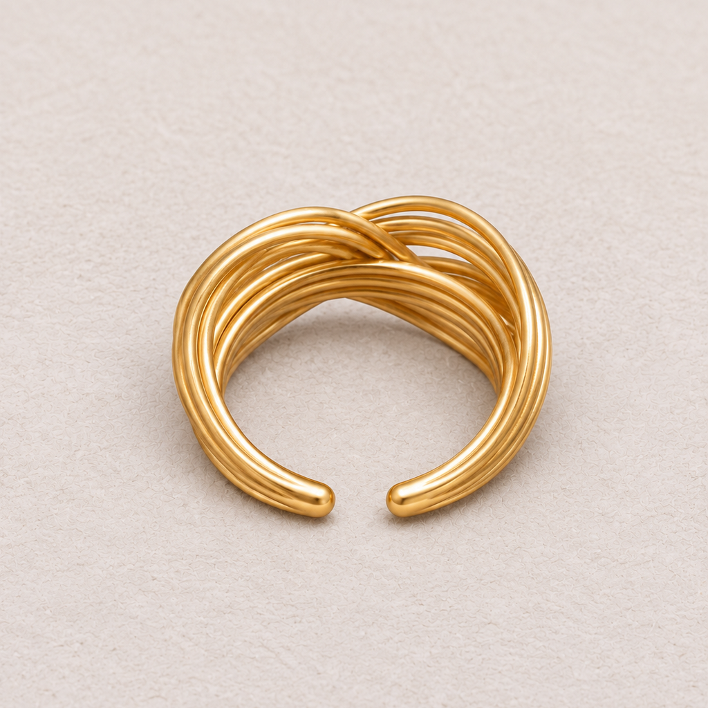 A gold-toned open cuff ring with a twisted, rope-like design, photographed on a neutral textured light beige background.