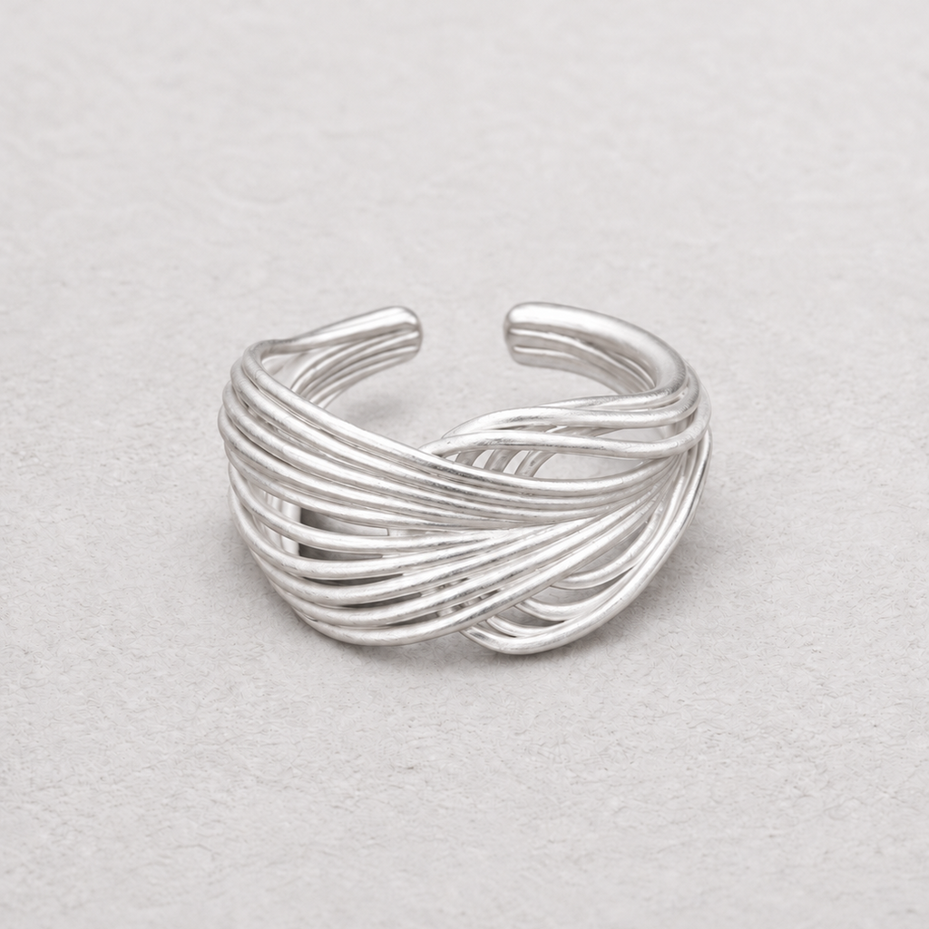 A silver-toned wrap ring with multiple twisted bands, photographed on a light textured neutral background.
