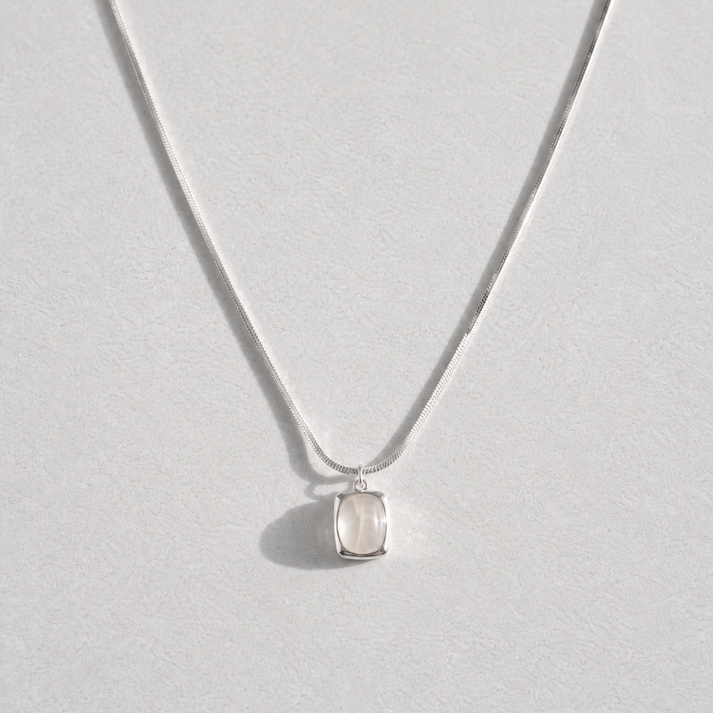 A delicate silver chain necklace with a small, bezel-set clear white agate gemstone pendant, displayed against a light gray background.
