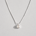 A delicate silver chain necklace with a small, bezel-set clear white agate gemstone pendant, displayed against a light gray background.