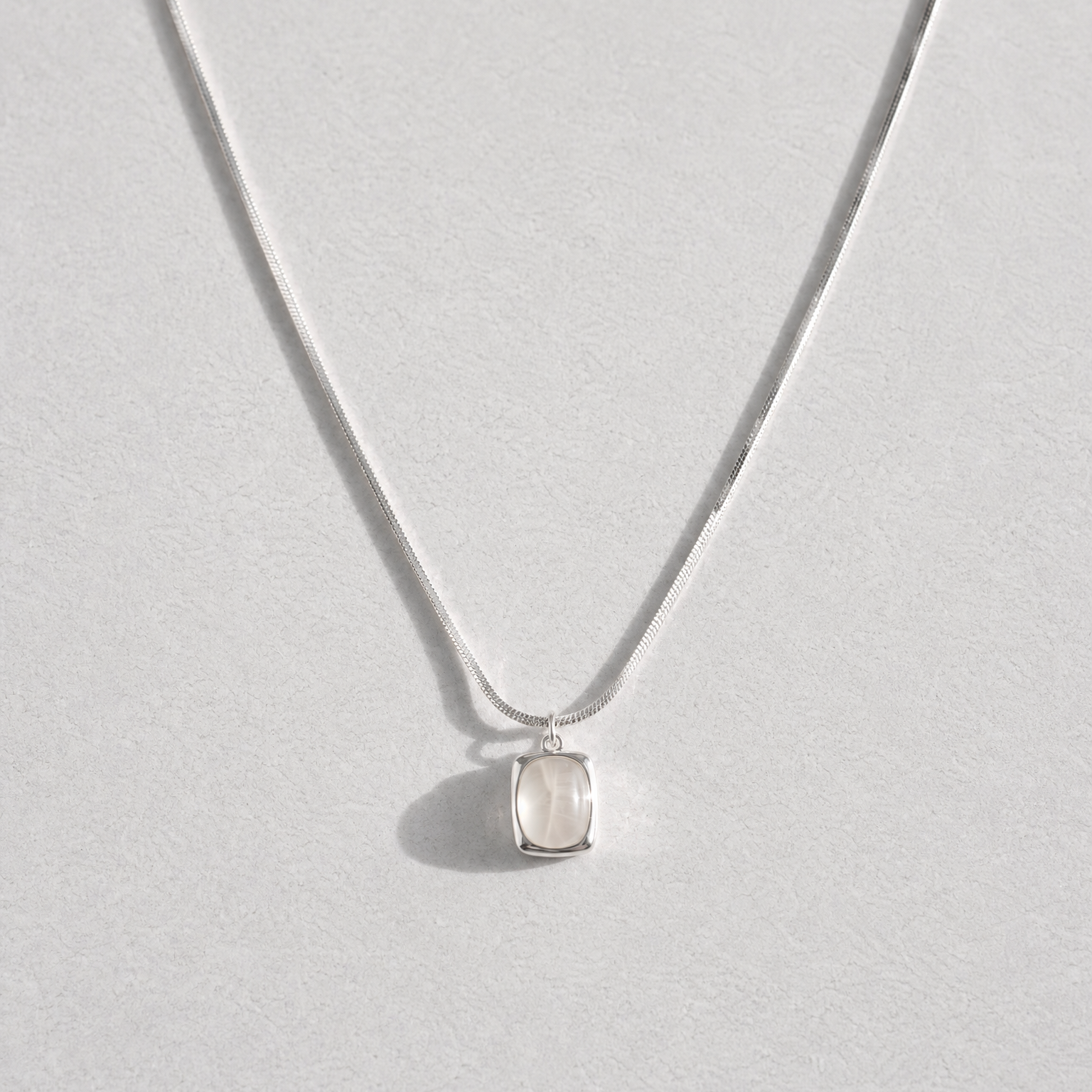 A delicate silver chain necklace with a small, bezel-set clear white agate gemstone pendant, displayed against a light gray background.