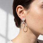 Close-up of a person wearing silver drop earrings with a neutral background