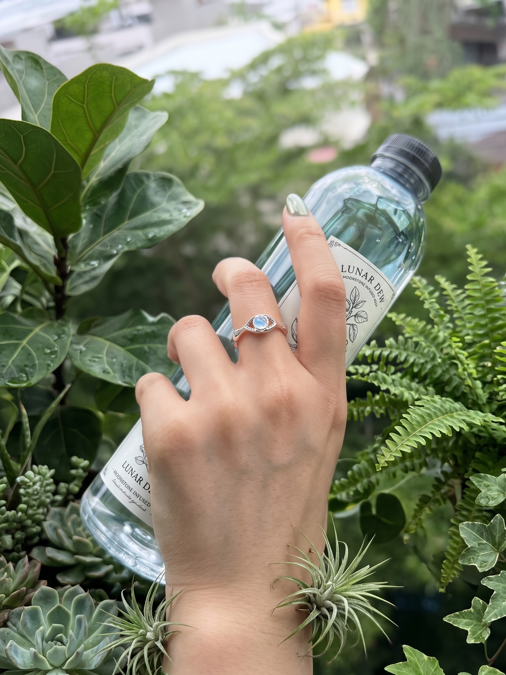 Hand wearing moonstone silver ring holding a water bottle with plants in the background