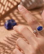 Hand wearing a blue gemstone ring on a textured surface with a blue stone.