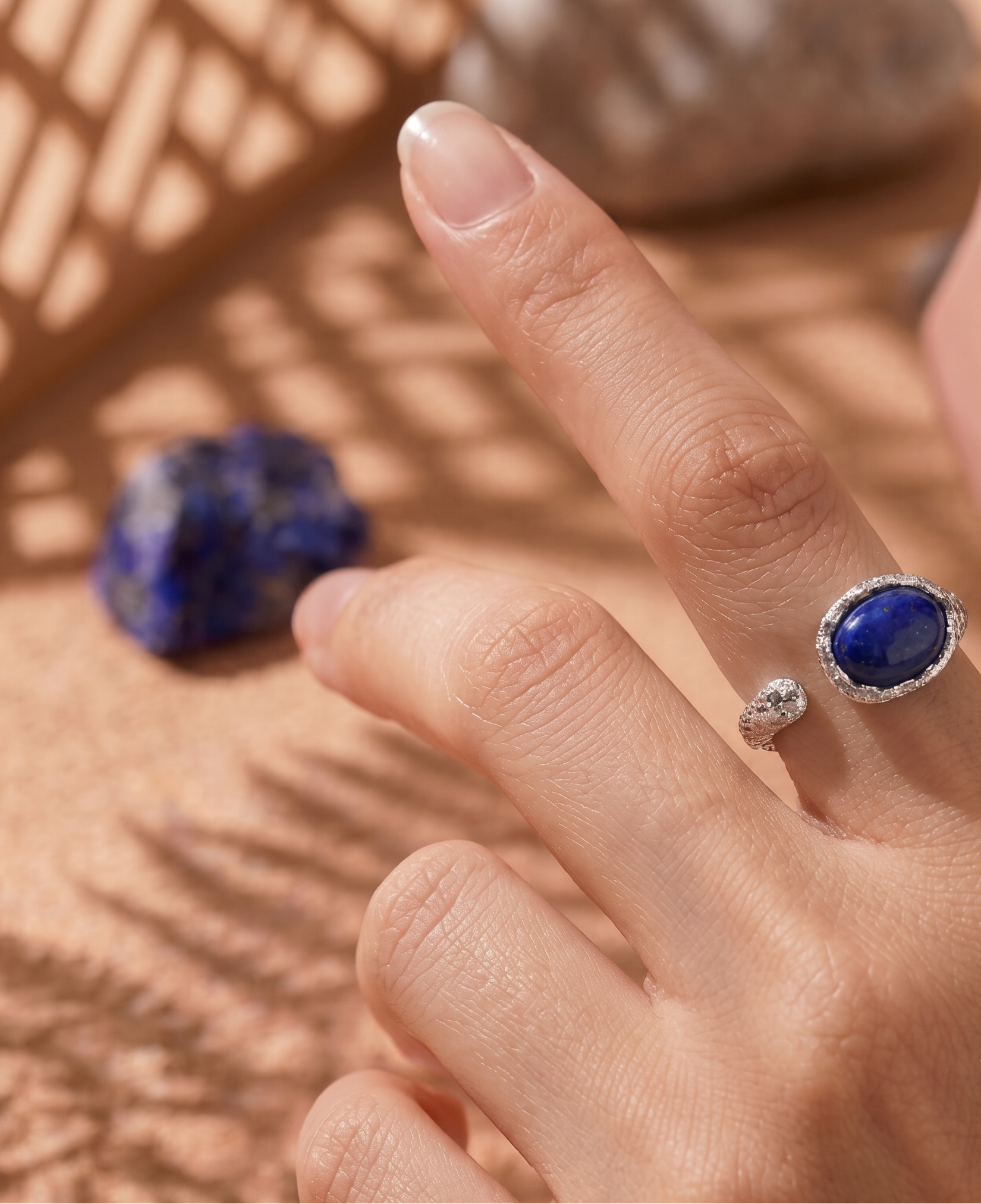 Hand wearing a blue gemstone ring on a textured surface with a blue stone.