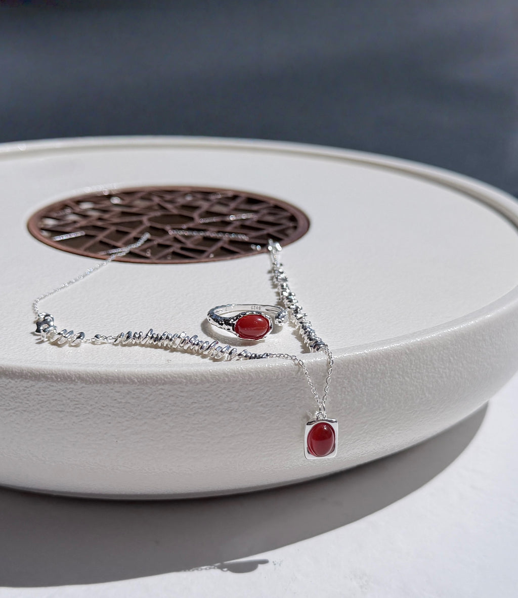 Silver necklace and ring with red agate stones on a white surface