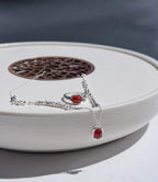 Silver necklace and ring with red agate stones on a white surface