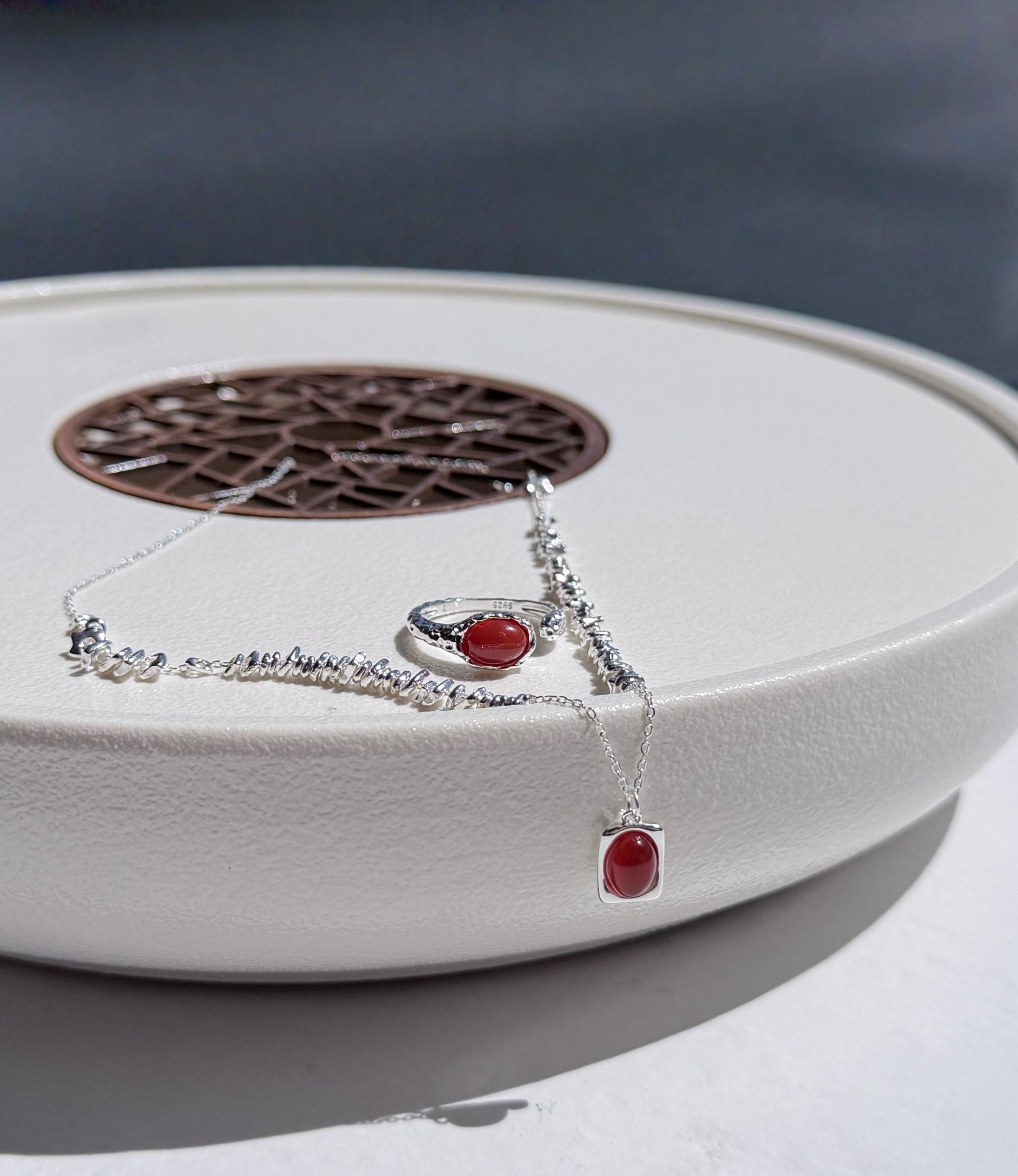 Silver necklace and ring with red agate stones on a white surface