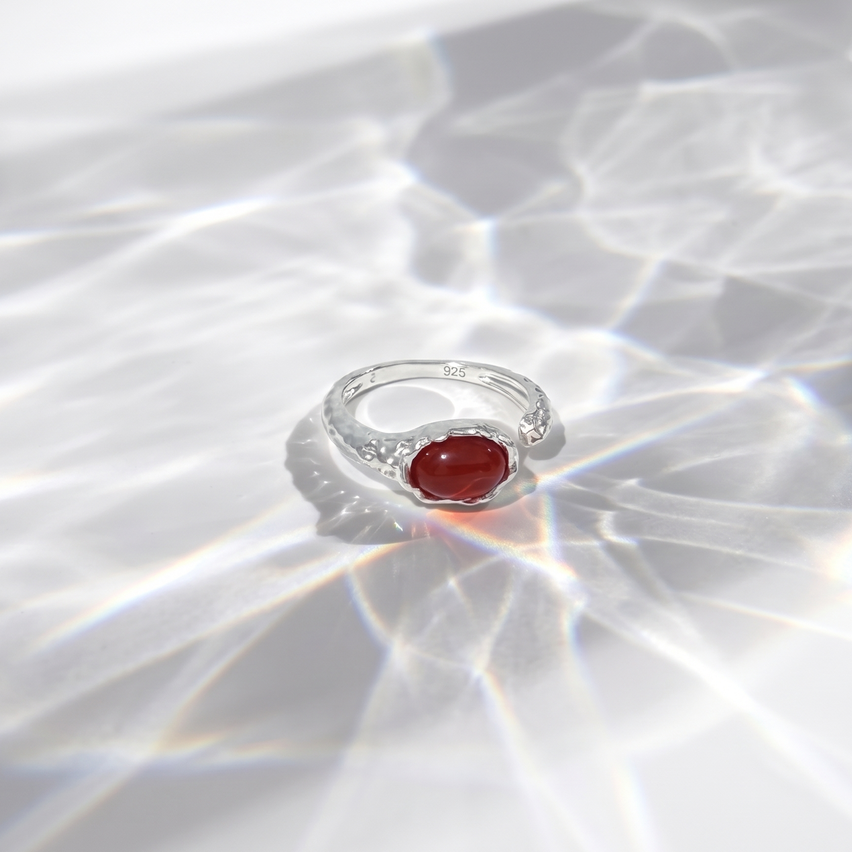 Silver ring with a red gemstone on a reflective white surface