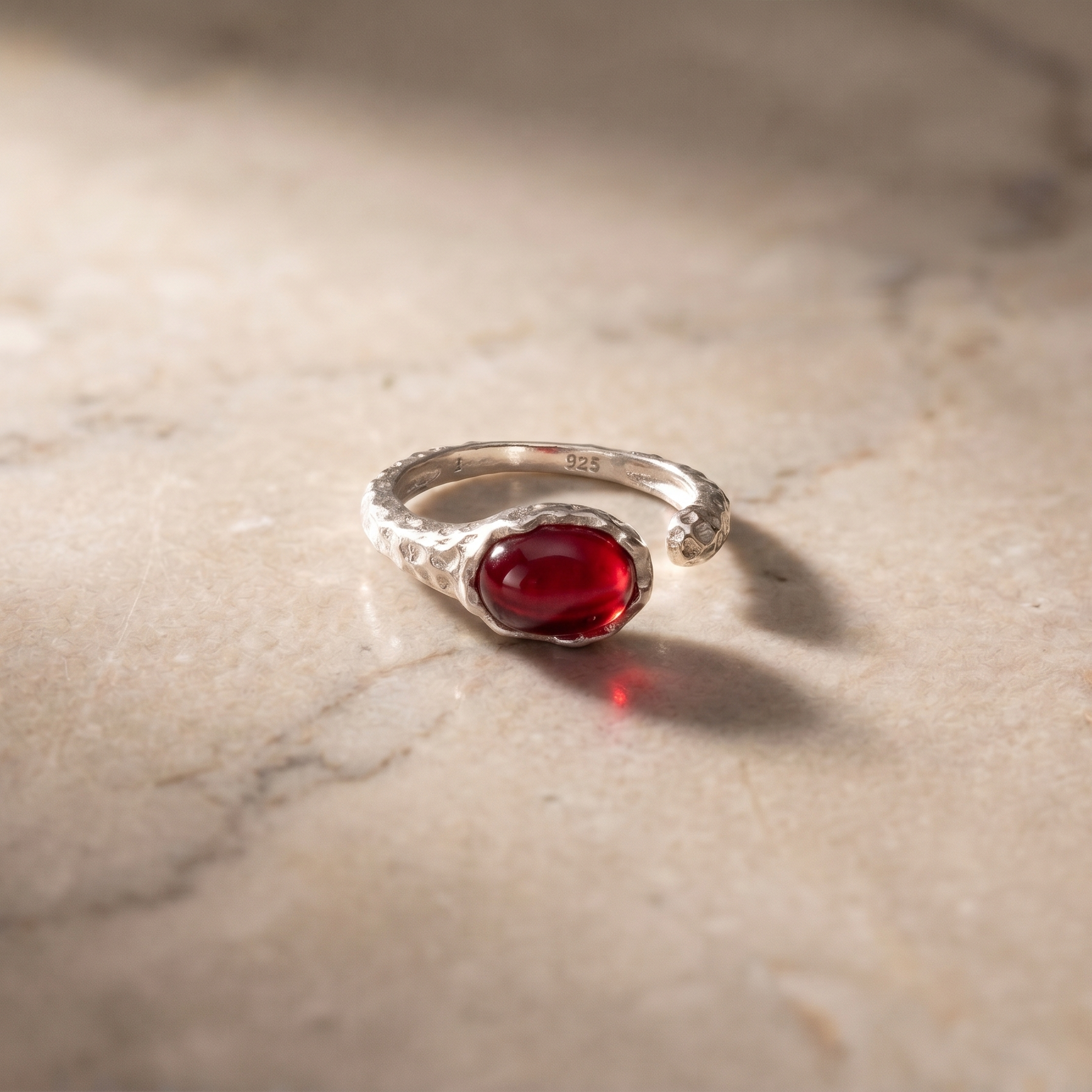 Silver ring with a red agate gemstone on a marble surface