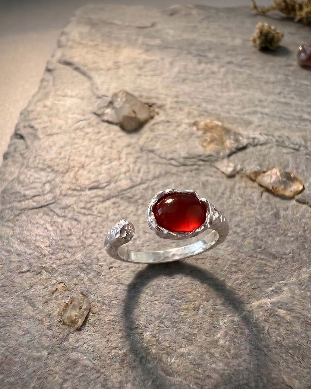 Silver ring with a red agate stone on a textured stone surface