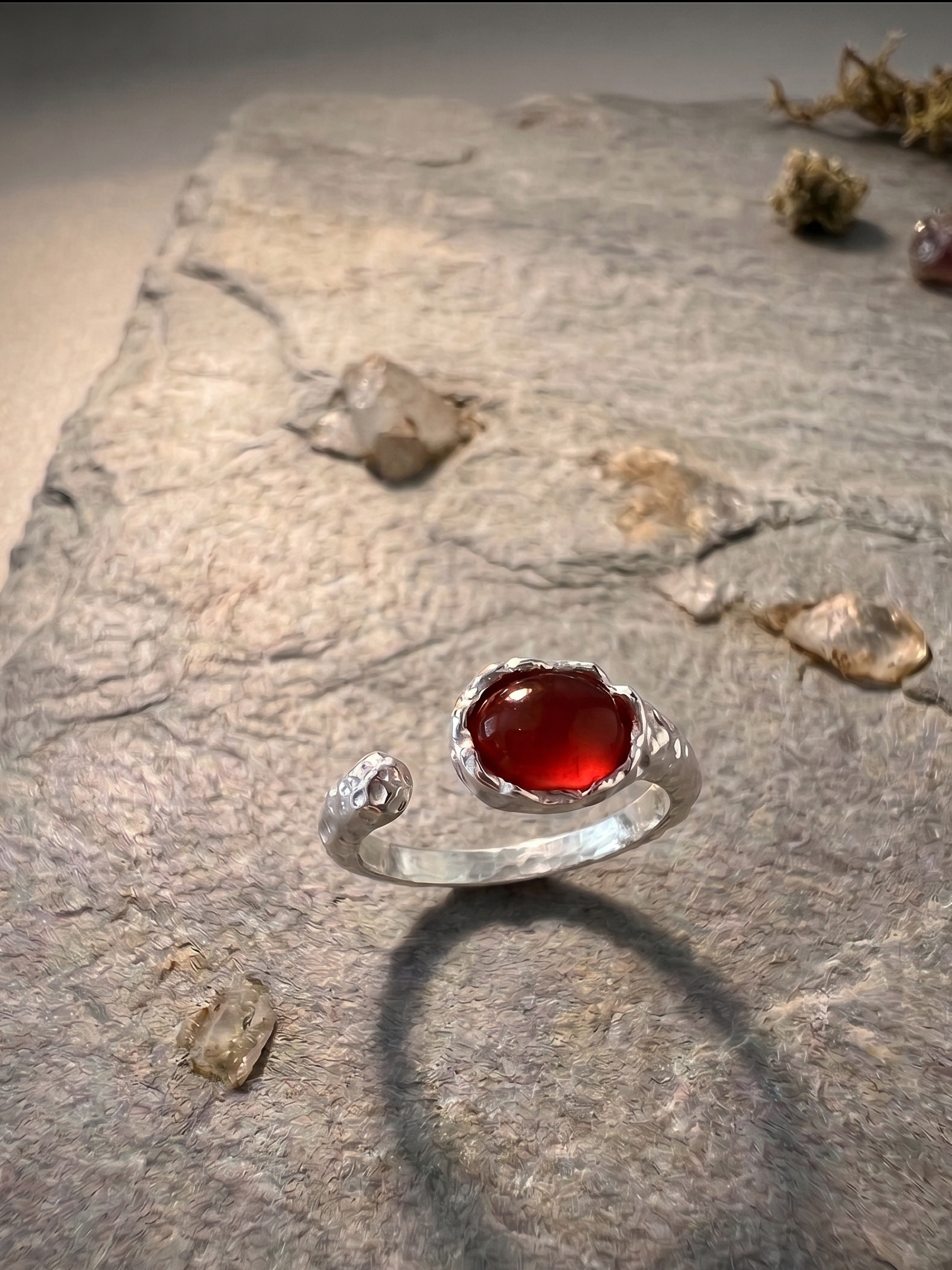 Silver ring with a red agate stone on a textured stone surface