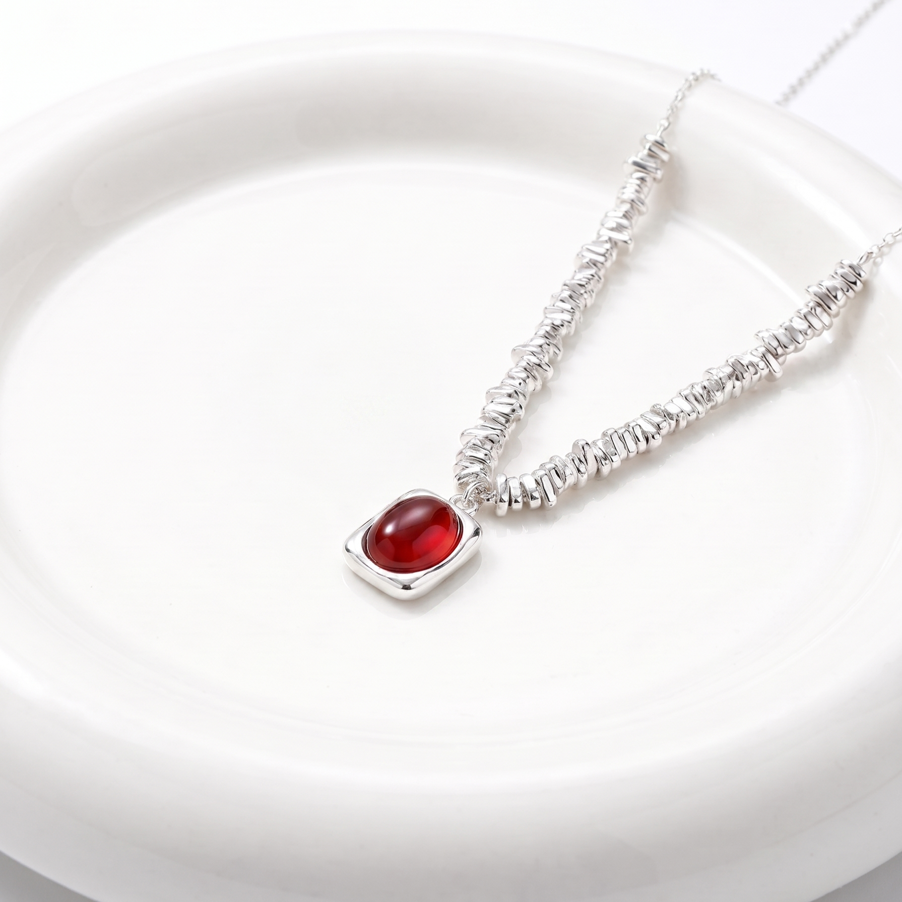 Silver necklace with a red agate stone on a white plate
