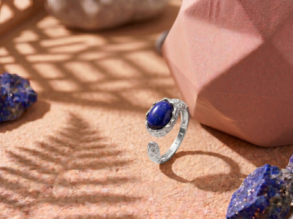 Silver ring with a blue gemstone on a textured surface with lapis lazuli stones.
