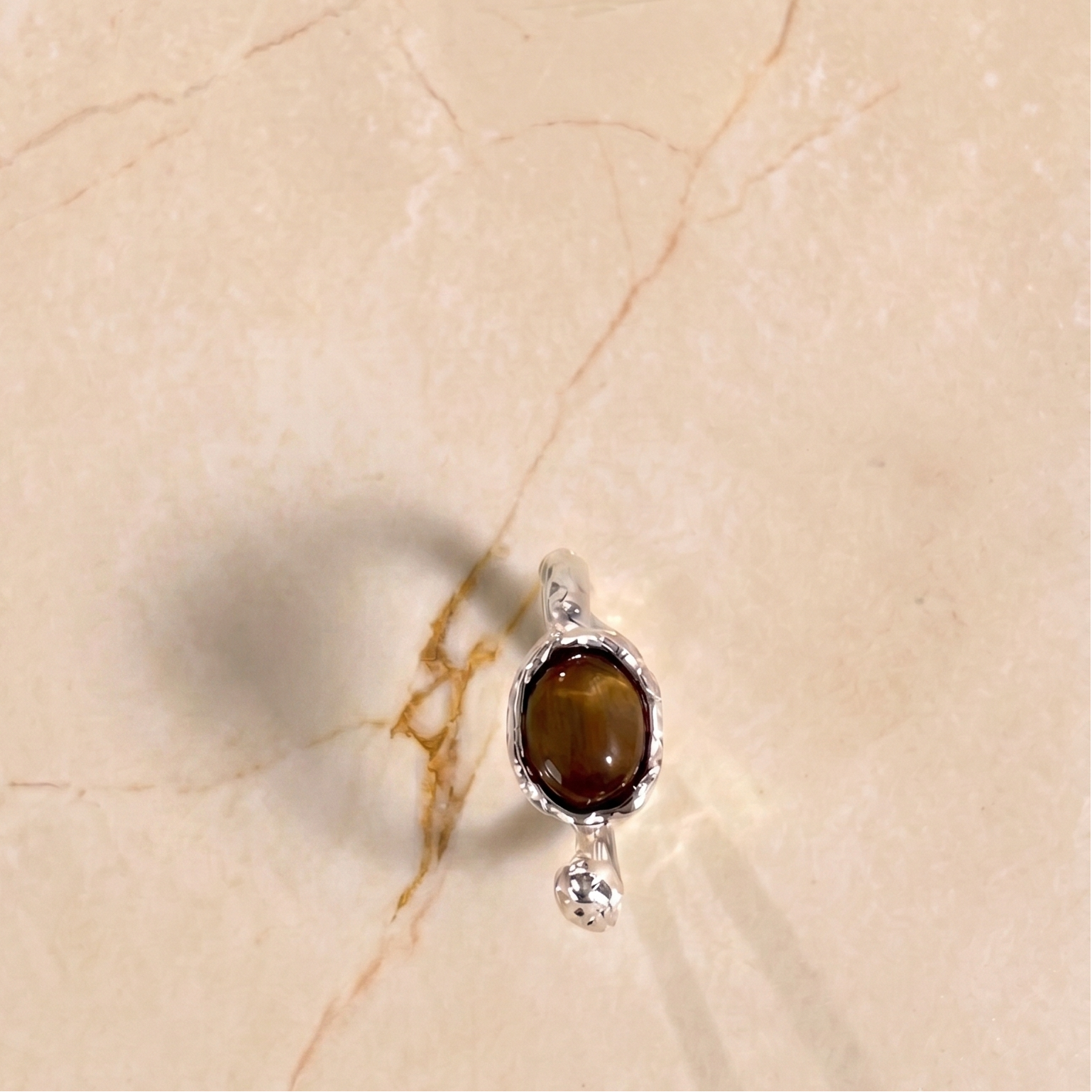Silver ring with a brown gemstone on a beige textured surface