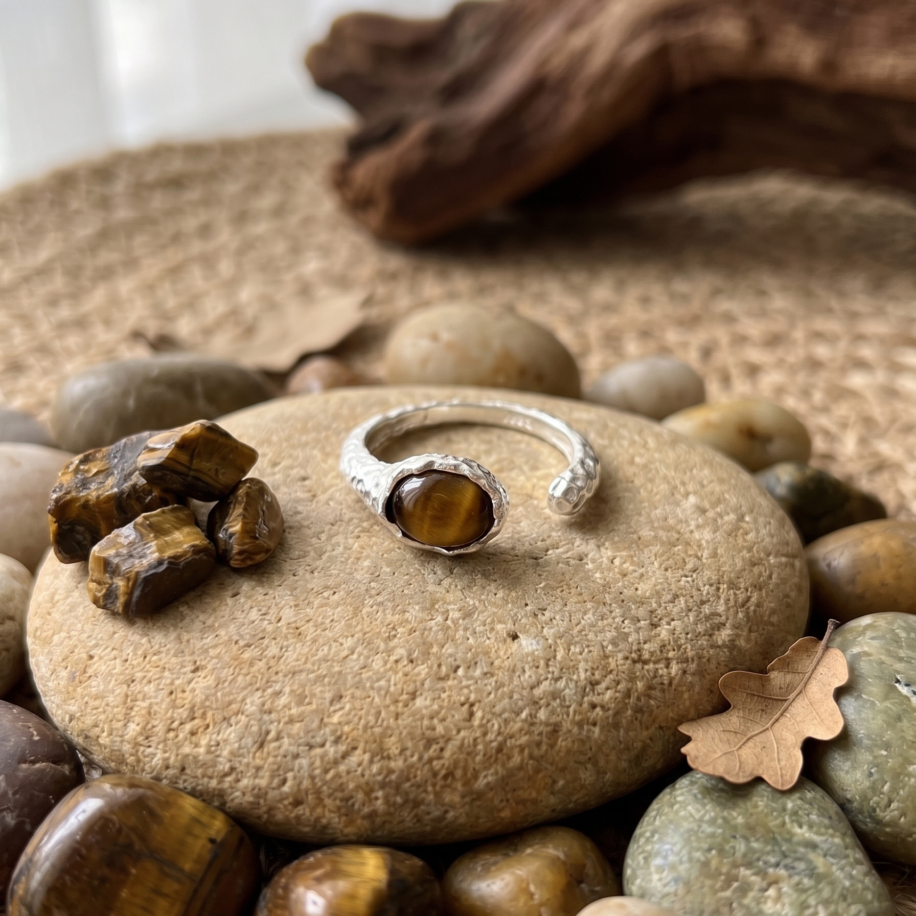 Silver ring with a tigereye gemstone on a stone surrounded by stones and driftwood