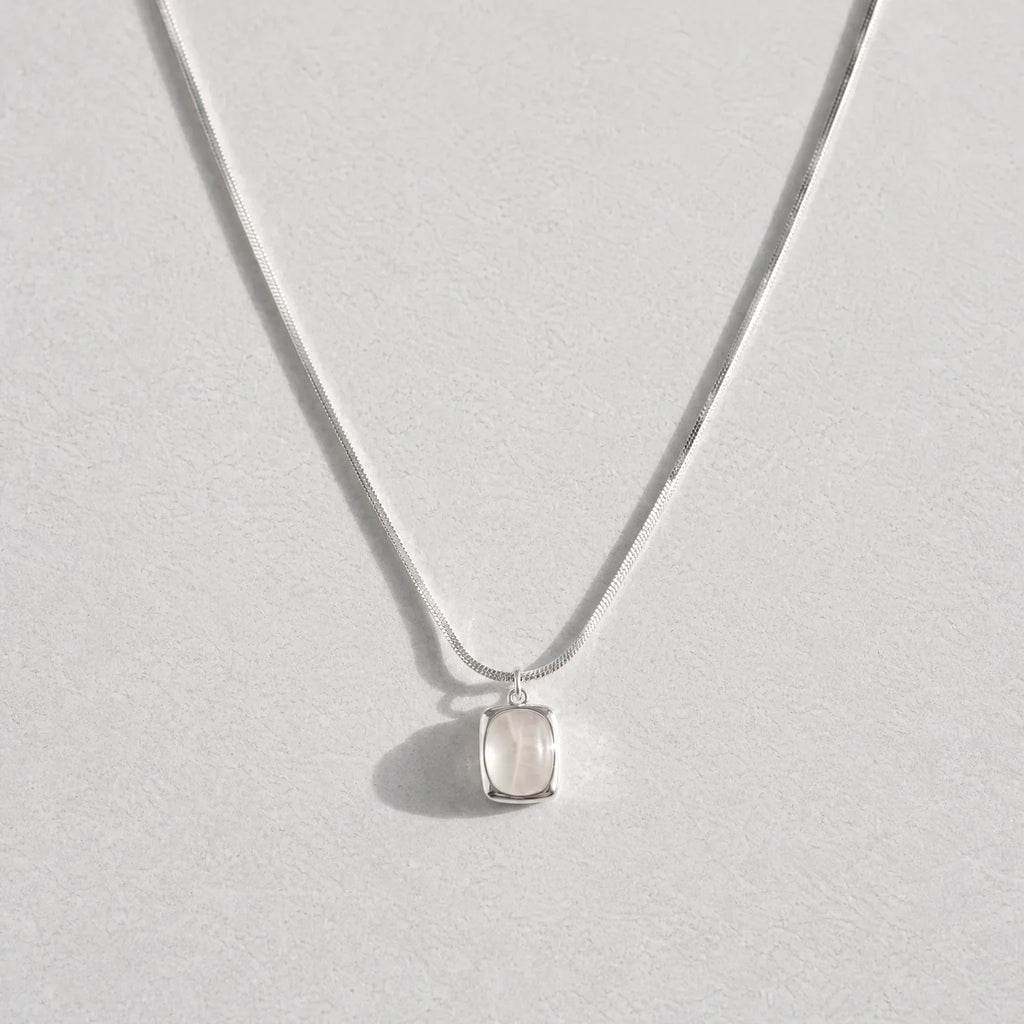 A delicate silver chain necklace with a small, bezel-set clear white agate gemstone pendant, displayed against a light gray background.
