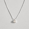 A delicate silver chain necklace with a small, bezel-set clear white agate gemstone pendant, displayed against a light gray background.