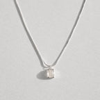 A delicate silver chain necklace with a small, bezel-set clear white agate gemstone pendant, displayed against a light gray background.