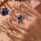 Hand wearing a ring with a blue gemstone on a textured surface