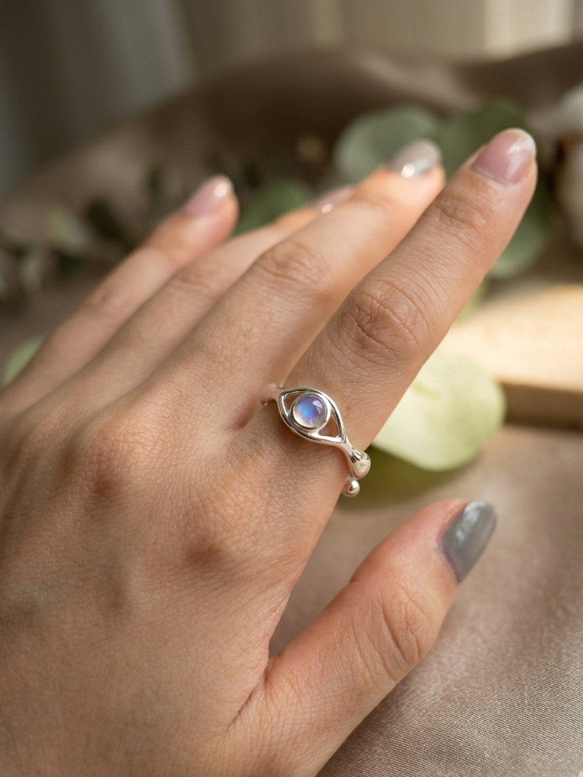 Hand wearing a silver ring with a moonstone on a neutral background