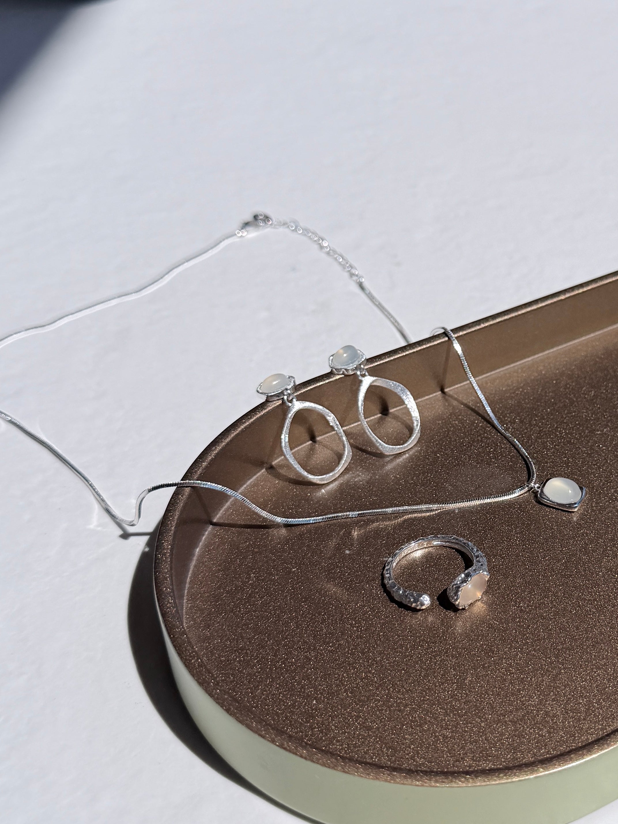 Silver white agate jewelry set including rings and earrings and a necklace on a textured surface