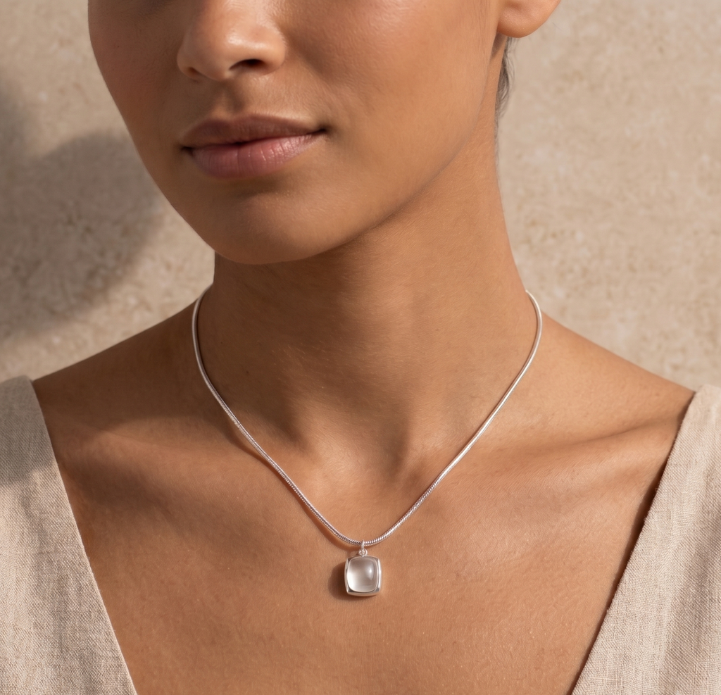 Close-up of a woman wearing a silver necklace with a white agate pendant against a neutral background