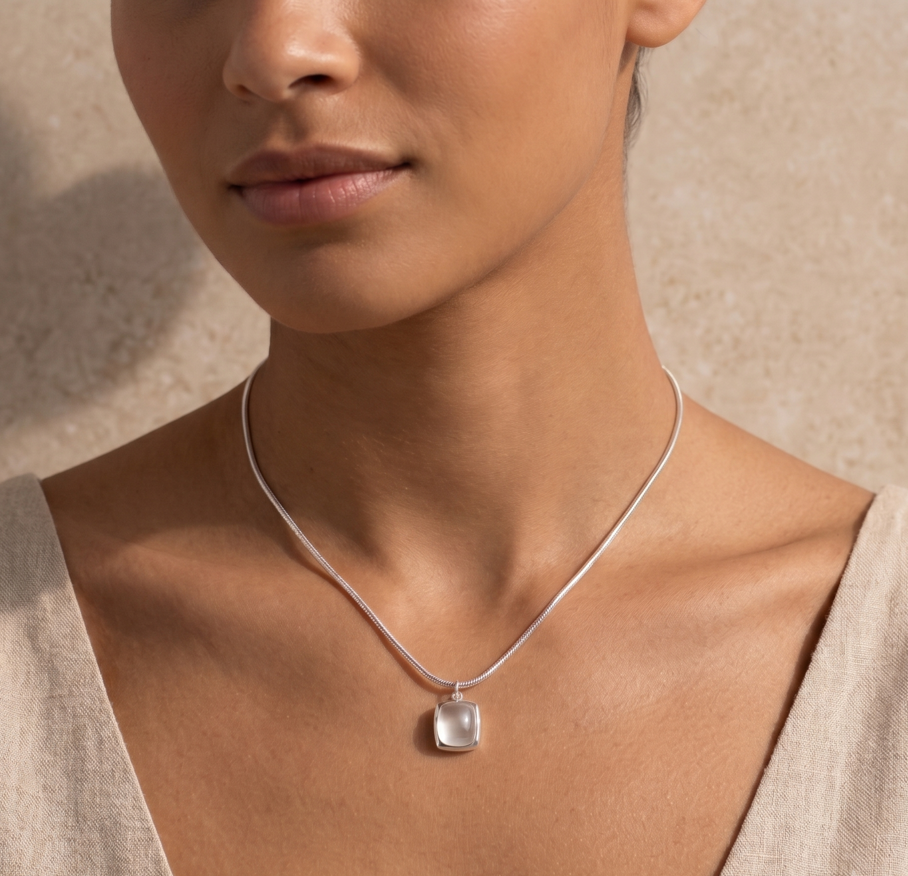 Close-up of a woman wearing a silver necklace with a white agate pendant against a neutral background